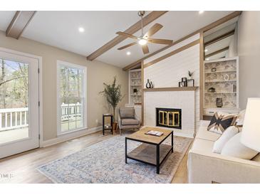 Cozy living room with fireplace, wood beams, ceiling fan, and built-in shelves with decorative wallpaper at 7825 Breckon Way, Raleigh, NC 27615