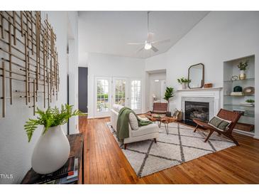Bright living room boasts a fireplace, hardwood floors, ceiling fan, and access to the outdoor deck through French doors at 6 Preakness Dr, Durham, NC 27713