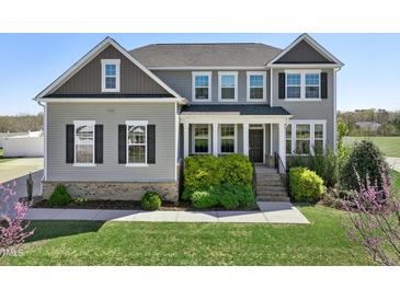Beautiful two-story home featuring a well-manicured lawn, lush landscaping, and a welcoming front porch at 834 November Ln, Willow Springs, NC 27592
