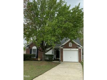 Charming brick home with a well-maintained lawn and a large tree providing shade at 144 Gremar Dr, Holly Springs, NC 27540