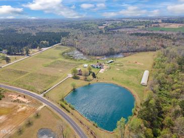 Expansive aerial view of a farmhouse featuring a large pond, pastures, and wooded areas creating a serene country estate at 97 Bailey Rd, Coats, NC 27521