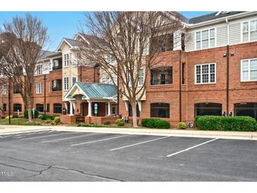 Brick apartment building featuring a covered entryway, manicured landscaping, and ample parking at 3700 Baron Cooper Pass # 104, Raleigh, NC 27612