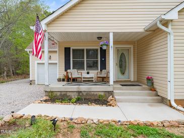 Charming front porch with seating area and an American flag displayed on a beige, single-story home at 104 Black Cloud Dr, Louisburg, NC 27549