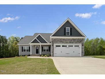 Charming home showcasing a stone-accented two-car garage, gray siding, and a well-manicured lawn on a sunny day at 106 S Harper Faith Way, Benson, NC 27504