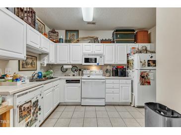 Well-lit kitchen with white cabinets, appliances, and light tile flooring with décor at 2521 Friedland Pl # 201, Raleigh, NC 27617