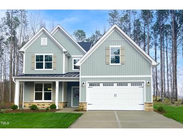 Charming two-story home with a light blue exterior, stone accents, well-manicured lawn, and attached two-car garage at 9512 Wood River Dr, Zebulon, NC 27597