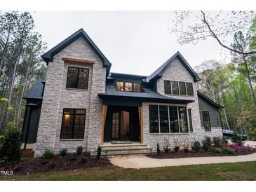 Stunning stone home with black trim, complemented by lush landscaping at 2200 Paddstowe Main Way, Wake Forest, NC 27587
