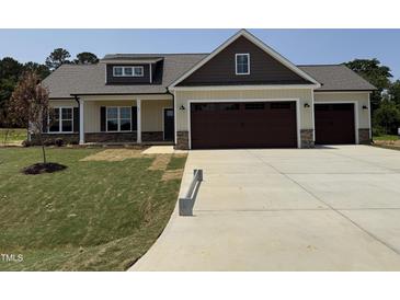 Charming home featuring tan siding, stone accents, a three-car garage, and manicured lawn at 87 Tee Dr, Selma, NC 27576