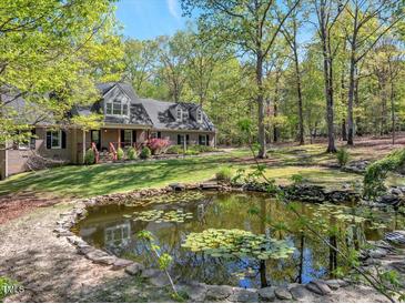 Charming brick home featuring a pond with lily pads, lush greenery, and mature trees surrounding the property at 363 Dublin Dr, Sanford, NC 27330