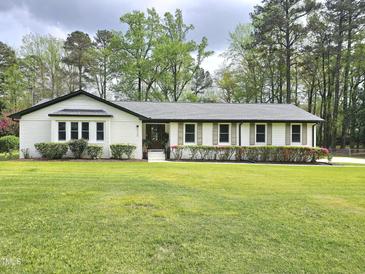 Charming single-story home featuring white brick and siding, complemented by a well-maintained green lawn and mature trees at 5920 Holly Dr, Raleigh, NC 27616