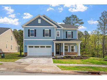 Charming two-story home with blue siding, a covered porch, and a two-car garage in a lush landscape at 5209 Woodlawn Dr, Durham, NC 27703