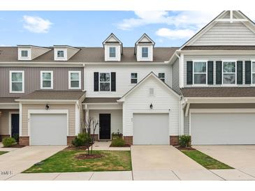 View of townhome exteriors showing the garages and small landscaped front lawns under a cloudy blue sky at 95 Little Leaf Lane Ln, Clayton, NC 27527