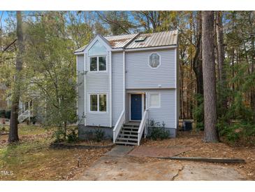 Charming two-story home featuring a blue front door, unique windows, and a metal roof surrounded by a wooded area at 19 Lansgate Ct, Durham, NC 27713