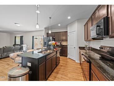 A kitchen boasts a central island with barstool seating and sleek, modern appliances on wood-look floors at 95 Shady Creek Trl, Garner, NC 27529