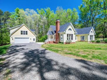 Charming yellow home featuring a brick chimney, a garage, and a well-maintained lawn and gravel driveway at 1208 Goodwin Rd, Apex, NC 27523