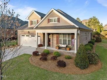Charming brick home featuring a two-car garage, a cozy front porch with bench, and well-maintained landscaping at 5733 Mizuno Dr, Fuquay Varina, NC 27526