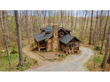 A beautiful log home nestled in the woods with a stone chimney and inviting porches at 2931 Western Hills Ln, Elon, NC 27244