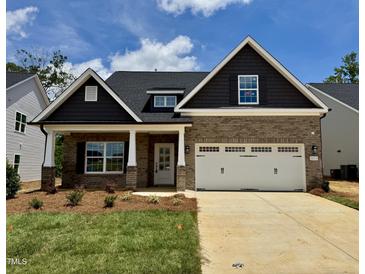 Charming brick home with a two-car garage, covered porch, and beautifully landscaped front yard under a blue sky at 1075 Fairhaven Dr # 51, Mebane, NC 27302