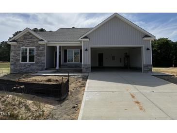 New construction featuring a two-car garage, stone accents and gray vinyl siding, with an unfinished yard at 69 Tee Dr, Selma, NC 27576