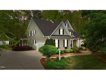 Charming two-story home with a well-manicured lawn, lush greenery, and a private driveway leading to an attached garage at 144 W Walker Woods Ln, Clayton, NC 27527