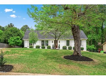 Charming white home featuring a lush, green lawn and mature trees under a bright blue sky at 5712 Wintergreen Dr, Raleigh, NC 27609