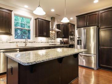 A modern kitchen with dark cabinets, stainless steel appliances, and a large island with granite countertops at 65 N Wilders Ridge Way, Clayton, NC 27527