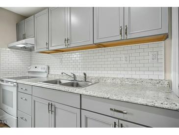 Modern kitchen with gray cabinets, stainless steel sink, granite countertops, and white subway tile backsplash at 500 John St St, Clayton, NC 27520