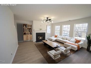 Bright living room features a fireplace, modern light fixture, and ample natural light from the many surrounding windows at 3244 Marcony Way, Raleigh, NC 27610