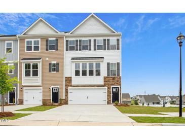 Attractive townhome featuring a two-car garage, stone accents, and a well-manicured lawn at 743 Parc Townes Dr # 36, Wendell, NC 27591