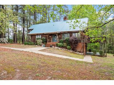 Charming home featuring a metal roof, lush landscaping, and a walkway through the trees to the back at 1355 Bowling Road, Fuquay Varina, NC 27526