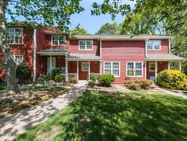 Charming red townhome featuring a well-manicured lawn, inviting front porch, and lush landscaping at 116 Old Maple Ln, Durham, NC 27713