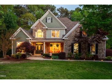Charming stone and shake siding home featuring a welcoming front porch and meticulously landscaped front yard at twilight at 8480 Falkirk Ridge Ct, Wake Forest, NC 27587