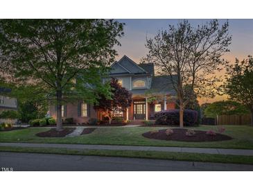 Charming brick home featuring a well-manicured front yard with lush landscaping and mature trees at dusk at 149 Country Mill Way, Fuquay Varina, NC 27526