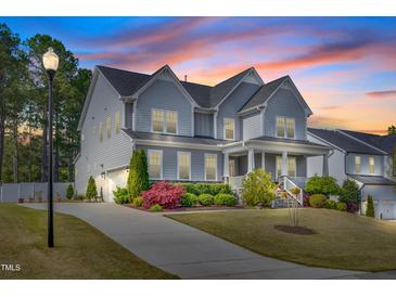 Beautiful two-story home featuring a welcoming front porch and lush landscaping at sunset at 3037 Freeman Farm Way, Rolesville, NC 27571