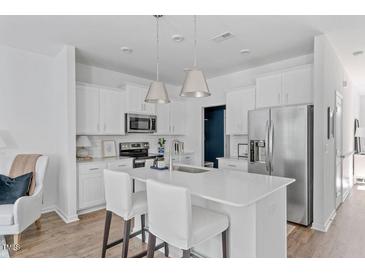 Bright, eat-in kitchen features stainless appliances, white cabinets, a center island with seating, and pendant lights at 3667 Durwood Ln, Raleigh, NC 27604