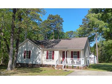 Charming single-story home featuring red shutters, a covered porch, and lush surrounding trees at 334 Cabin Grove Ct, Angier, NC 27501