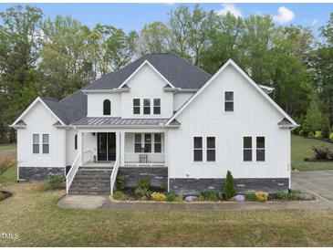 Charming two-story white home featuring stone accents, a welcoming front porch, and lush landscaping at 6024 Lunenburg Dr, Raleigh, NC 27603