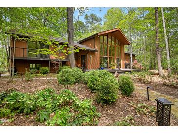 A beautiful brown home featuring a wall of windows, a wooden deck, and lush green landscaping at 673 Brookview Dr, Chapel Hill, NC 27514