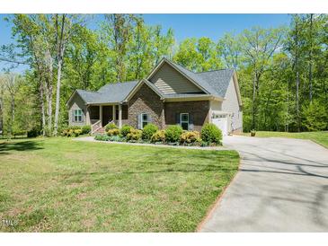 Inviting single-story home featuring stone accents, well-maintained landscaping, and a paved driveway on a sunny day at 4057 Mackenzie Dr, Haw River, NC 27258