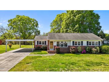 Charming brick home featuring a lush green lawn, flowering bushes, and convenient covered carport at 1802 Prince Edward Dr, Elon, NC 27244