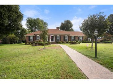 Charming brick home with a walkway, manicured lawn, and mature trees under a blue sky at 705 N Gurney St, Burlington, NC 27215