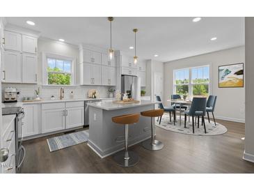 Bright kitchen featuring white cabinets, stainless steel appliances, island with bar stools, and adjacent dining area at 241 Connelly Way, Zebulon, NC 27597