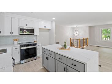 Bright kitchen features gray island, stainless steel appliances, white cabinets, and access to the living room at 1514 Goodwin Rd, Durham, NC 27712