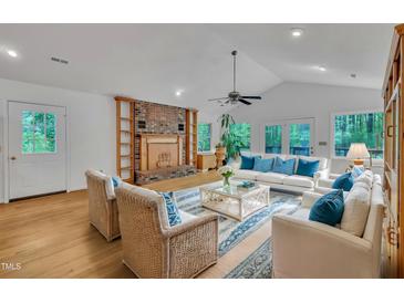 Bright living room with vaulted ceilings, brick fireplace, hardwood floors and white furnishings with blue accents at 480 Big Branch Dr, Pittsboro, NC 27312
