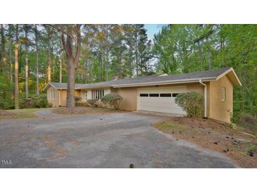 Charming brick ranch-style home with attached garage and circular driveway nestled among mature trees at 110 Omega Rd, Henderson, NC 27536
