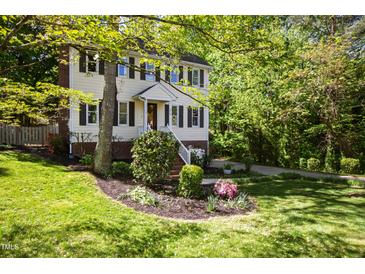 Charming two-story home with light yellow siding, black shutters, brick foundation and lush landscaping at 213 Beechtree Dr, Cary, NC 27513