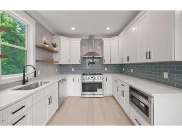 Bright kitchen with white cabinets, stainless steel appliances, light wood floors, and blue tiled backsplash at 621 Bon Air Ave, Durham, NC 27704