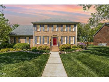 Stunning brick home with a manicured lawn, beautiful landscaping, and a welcoming red front door at 2545 Churchill Dr, Burlington, NC 27215