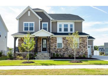 Beautiful two-story home featuring stone accents, a welcoming front porch and lush green lawn on a sunny day at 213 North Crest Dr, Chapel Hill, NC 27517