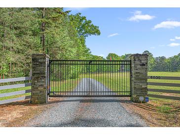 Gated entrance to a beautiful property with mature trees and a long gravel driveway leading to the home at 6600 Maynard Farm Rd, Chapel Hill, NC 27516